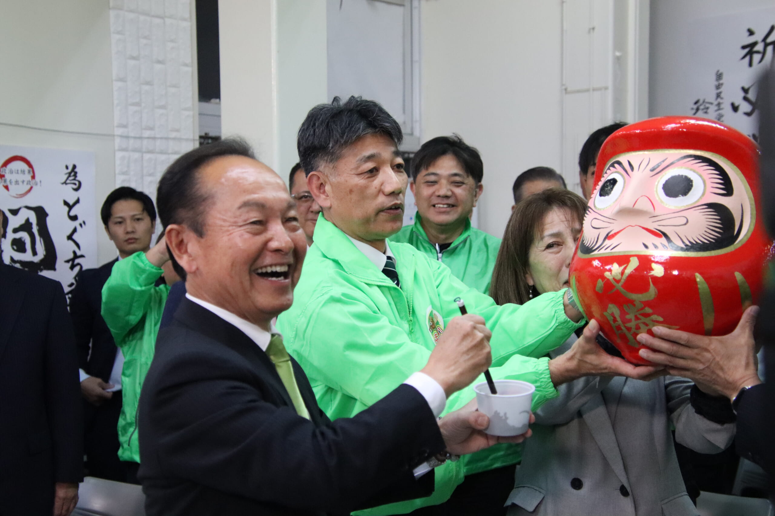 笑顔でだるまの目を描き入れた渡具知氏＝25日夜、名護市